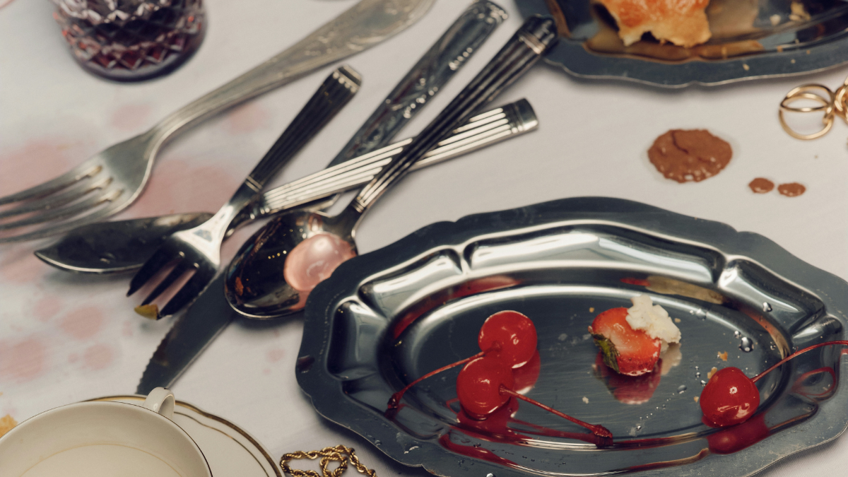 Close-up of a silver dessert plate with cherries and scattered cutlery on a restaurant table after a meal