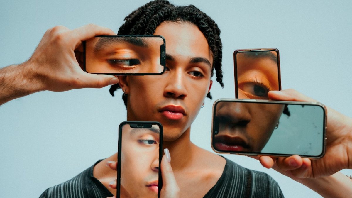 Person surrounded by multiple smartphones reflecting their face, representing AI-generated identity and digital visibility