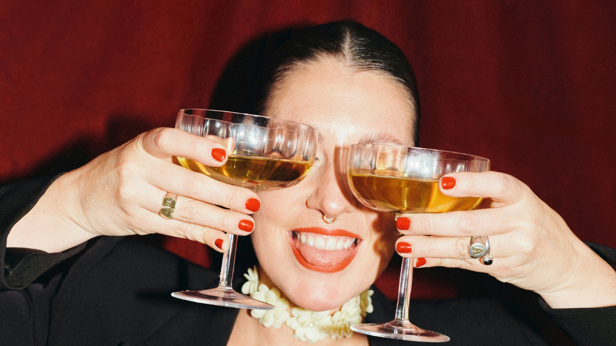 Woman smiling and holding two coupe glasses in front of her face at a restaurant or bar event