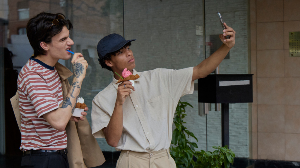 Two young people eating ice cream on the street, one taking a selfie with a smartphone